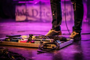 A pedal board with a guitarist behind it plugged in on stage