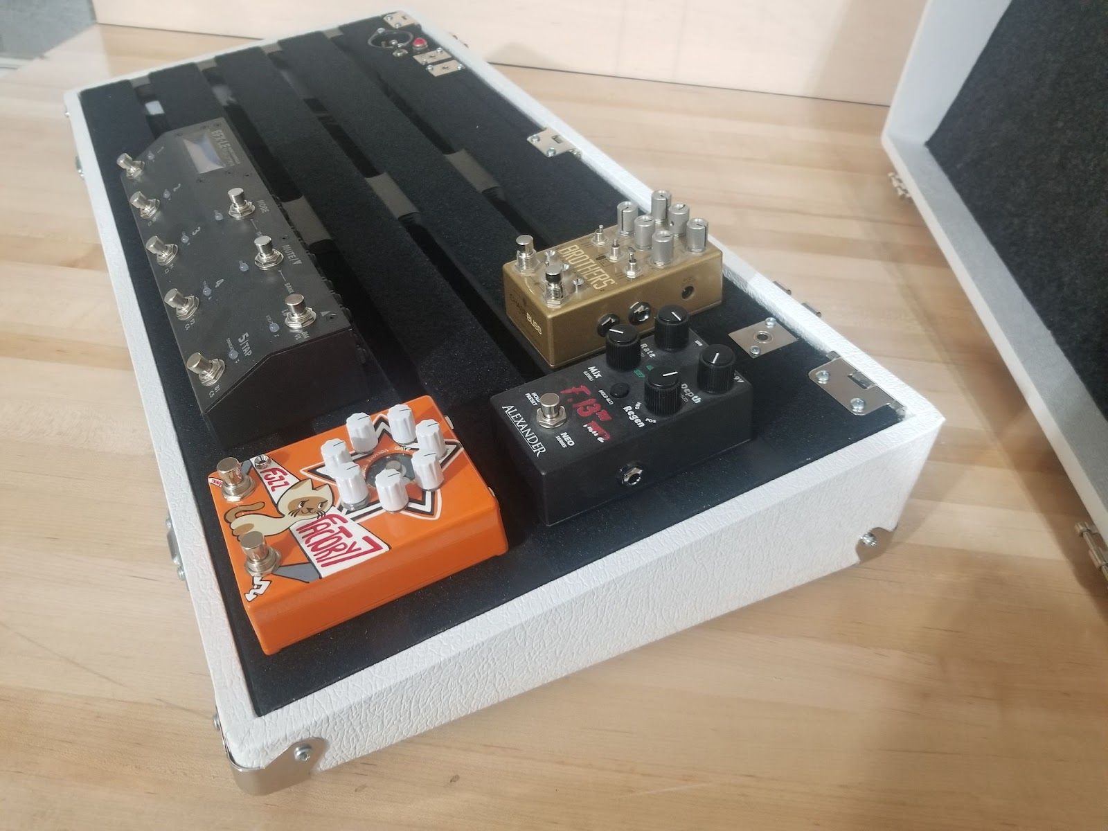 A white Pedal Pad custom pedal board with four different effects pedals placed on top